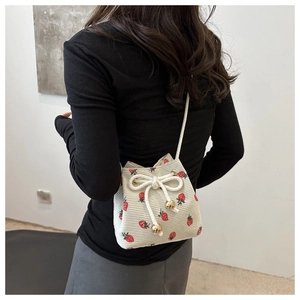 Detail of strawberry print corduroy bucket bag featuring cream fabric and gold metal charms