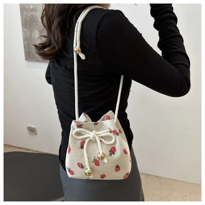 Detail of cream corduroy bucket bag with red strawberry print and golden drawstring beads