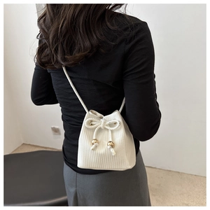 Back view of a model wearing a mini white woven bucket bag with gold bead drawstrings