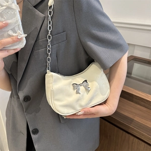 Cream crescent shoulder bag with silver bow accent and metallic chain strap worn with blazer