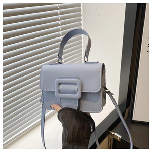 Detailed view of light blue crossbody bag with large buckle and soft shadow lighting