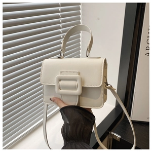Close-up of white minimalist flap handbag with decorative buckle and slim shoulder strap