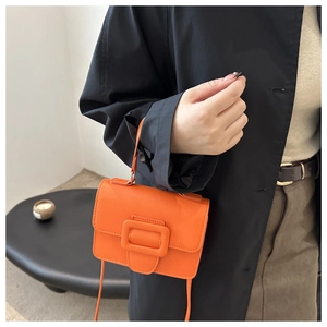 Detail shot of bright orange square handbag with leather flap and large buckle accent