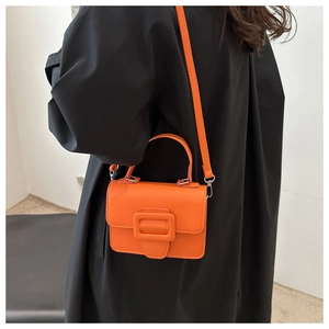Détail d'un mini sac à main orange vif avec boucle carrée sur une tenue de manteau noir