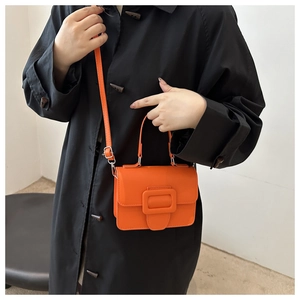 Détail du sac bandoulière orange vif avec boucle argentée sur fond de manteau noir