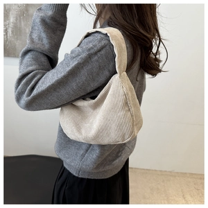 Detail of cream corduroy shoulder bag showing texture and fit on a model in grey sweater