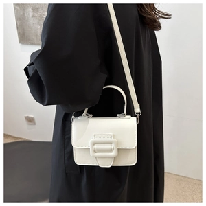 Détail d'un sac à main blanc minimaliste avec grande boucle sur un manteau noir élégant