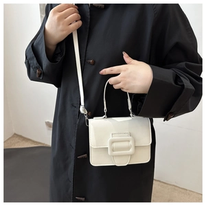 Vue détaillée du sac à main blanc brillant avec boucle carrée sur un manteau noir élégant