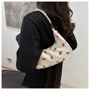 Detail of white corduroy shoulder bag featuring red strawberry prints and pearl chain strap