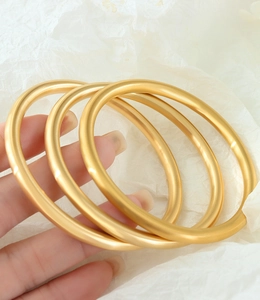 Detailed view of three matte gold-plated bangles in durable 18K titanium steel finish