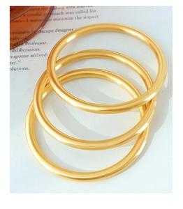 Detailed view of three minimalist matte gold bangles stacked on a magazine background