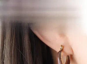 Nahaufnahme eines Models mit braunen Emaille-Creolen in V-Form und Goldrand-Design