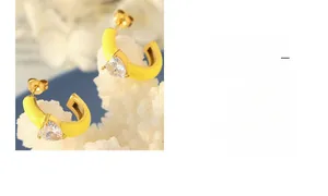 Makroaufnahme gelber Emaille-Ohrringe in C-Form mit Zirkonia-Herz und Gold-Finish