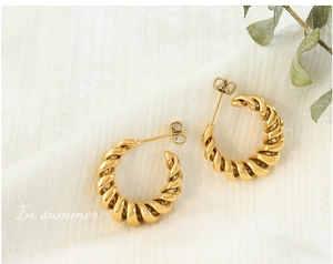 Detail of gold twisted croissant hoop earrings on white fabric with summer leaves