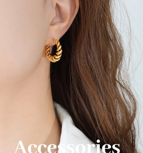 Close-up of golden croissant twist hoop earrings worn by a model with metallic texture