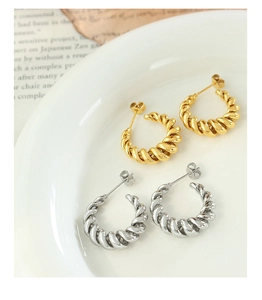 Close-up of gold and silver twisted rope C-shaped earrings on a vintage paper background