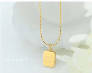 Macro detail of gold square pendant with CHARM engraving on polished chain necklace