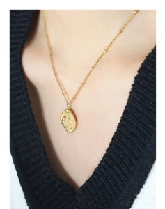 Detail of gold satellite chain necklace featuring an oval engraved figure pendant on a model