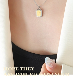 Gros plan d'un collier pendentif carré argent et or avec gravure Smile et visage