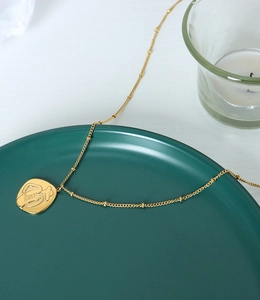 Detail of gold bead chain with square relief pendant on green ceramic plate