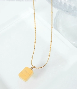 Macro view of a gold square charm necklace with a beaded chain and engraved charm detail