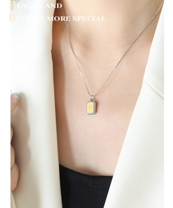 Détail d'un collier minimaliste bicolore avec un pendentif carré gravé d'un sourire
