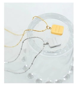 Detail of square charm necklace in gold and silver with engraved CHARM text on bead chain
