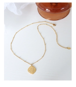 Macro detail of gold necklace with K18 engraving and abstract figure pendant