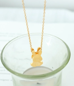 Gros plan d'un collier pendentif lapin doré suspendu sur un verre au décor épuré