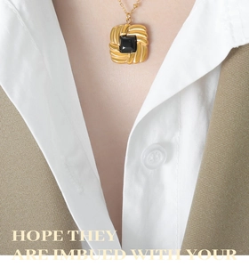 Close-up of golden necklace featuring a square black gemstone pendant with spiral texture