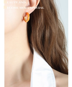 Detail view of stylish orange enamel and gold-plated C-shaped hoop earrings on a model