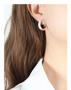 Close-up of white enamel and gold-plated C-shaped earrings worn by a model in bright light
