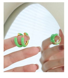 Detailed close-up of grass green enamel gold earrings held against a mirror