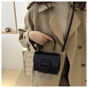 Détail d'un sac bandoulière noir en cuir avec grande boucle porté sur un trench-coat