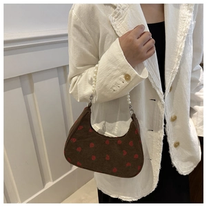Detail of brown corduroy baguette bag featuring red strawberry embroidery and pearl chain