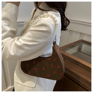 Detail of brown corduroy baguette bag with strawberry print and white pearl chain strap