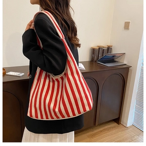 Détail macro du sac cabas en toile rayé rouge et blanc porté par un mannequin en scène