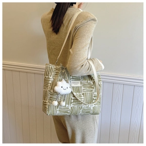 Detail of green and white woven tote bag with a cute cloud charm shown on model's shoulder