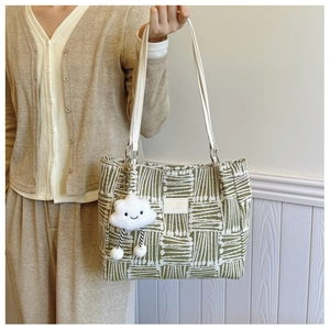 Detail of green woven tote bag with white leather strap and a plush cloud charm