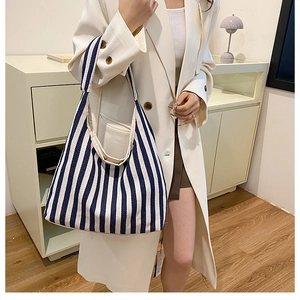 Gros plan d'un sac hobo en toile à rayures bleues et blanches porté par un mannequin