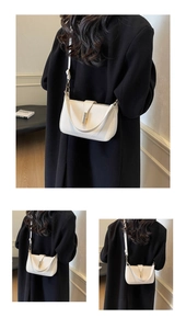 Detailed view of white leather crossbody bag with metal buckle on black coat background