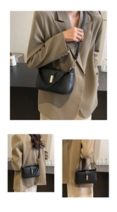 Detail of a black leather rectangular shoulder bag with golden metallic clasp buckle