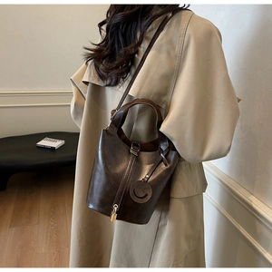 Détail d'un sac seau marron foncé brillant avec cadenas et charm sourire rond