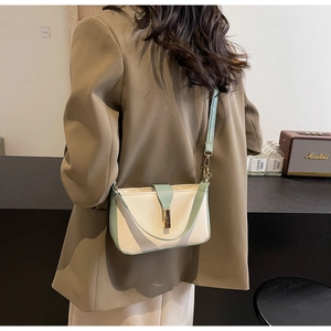 Detail shot of a mint green and beige crossbody bag with metal clasp on a model