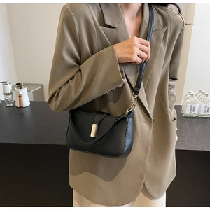 Close-up of black leather crossbody bag featuring a golden rectangular metal buckle