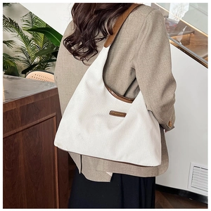 Detail of white corduroy tote bag with brown leather trim worn on the shoulder