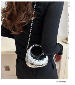 Detail of silver crescent chain bag with hammered metallic finish and mirror reflection