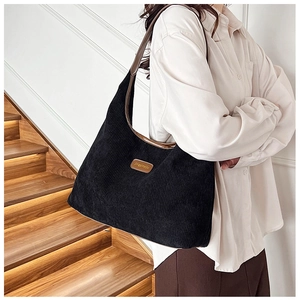 Detail of black corduroy tote bag with brown leather trim and shoulder strap worn by model