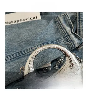 Detail view of silver textured mini bag with metallic chain and round handle on denim