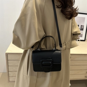Minimalist black flap crossbody bag with large square buckle shown with trench coat